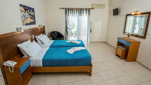 Et hotelværelse med to enkeltsenge dækket med blå sengetæpper og hvide lagner. (AI-genereret tekst)