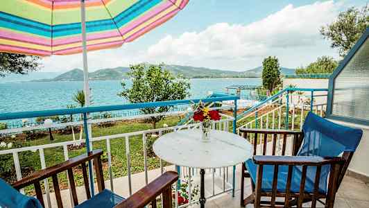 Udendørs område med bord, stole og en farverig parasol, med udsigt over havet og landskabet. (AI-genereret tekst)