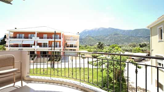 Udsigt fra en altan med en stol, en græsplæne og bygninger i baggrunden. (AI-genereret tekst)