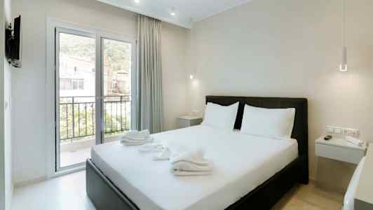 Et hotelværelse med en dobbeltseng, hvidt sengetøj og et vindue ud mod en balkon. (AI-genereret tekst)