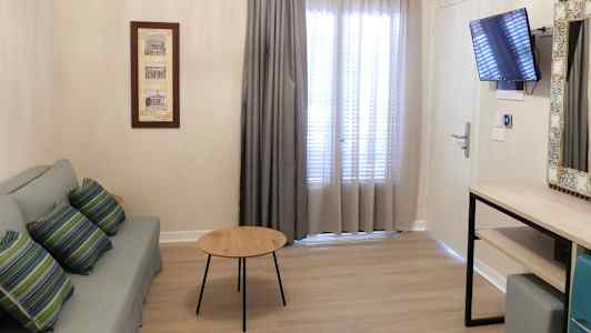 En stue med sofa, bord, gardiner foran vinduet, en vægmonteret tv og en kommode. (AI-genereret tekst)