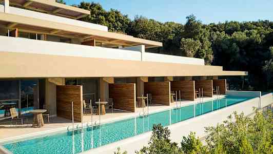 Udendørs pool ved hotelbygning med terrasse og afskærmede siddeområder. (AI-genereret tekst)