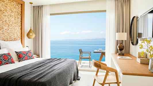 Et hotelværelse med en opredt seng, skrivebord og udsigt over havet gennem vinduet. (AI-genereret tekst)