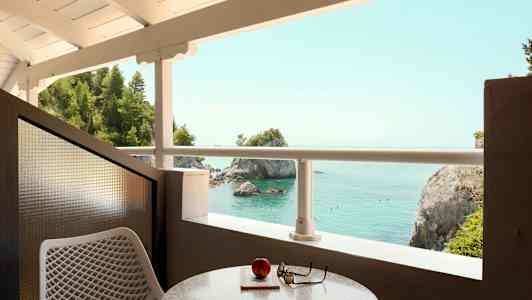 Udsigt fra en altan ud over havet med klipper og træer. (AI-genereret tekst)