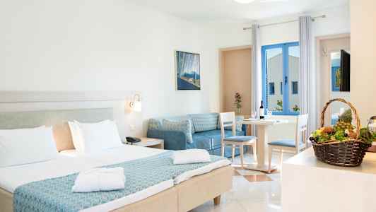 Et hotelværelse med dobbeltseng og siddeområde. En kurv med frugt står på et bord. (AI-genereret tekst)