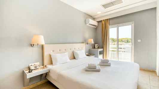 Moderne møbleret hotelværelse med dobbeltseng og hvide lagner. Vindue med lysindfald. (AI-genereret tekst)