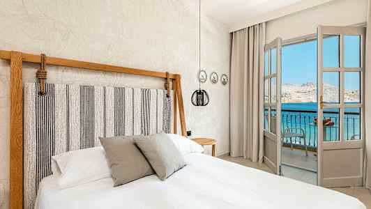 Soveværelse med en dobbeltseng og en åbning mod en balkon med udsigt over havet. (AI-genereret tekst)
