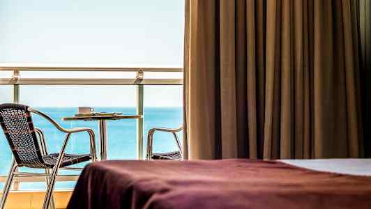 Værelse med brun gardin, udsigt over havet og møbleret altan. (AI-genereret tekst)