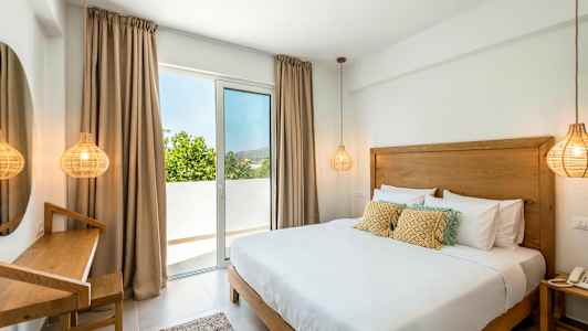 Værelse med en dobbeltseng, et skrivebordshjørne og et vindue, der fører ud til en balkon. (AI-genereret tekst)