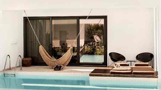 Billede af en pool med en hængekøje og liggestole ved kanten. (AI-genereret tekst)