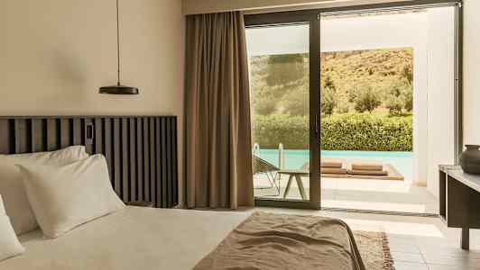 Et moderne hotelværelse med en stor seng, beige gardiner og en glasdør, der fører ud til en terrasse med pool. Udenfor ses grønne omgivelser og en skråning. (AI-genereret tekst)