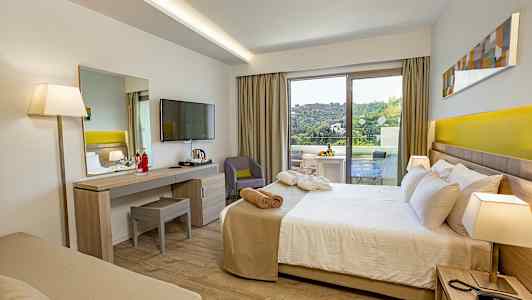 Et hotelværelse med seng, skrivebord, TV og en balkon med udsigt til grønne omgivelser. (AI-genereret tekst)