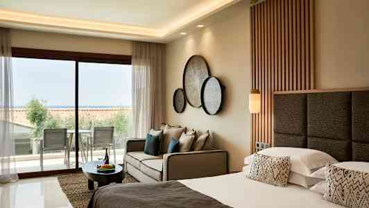 Billedet viser et moderne hotelværelse med dobbeltseng, sofa og udsigt til en altan. (AI-genereret tekst)