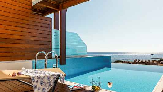 En infinity-pool med udsigt over havet, en liggestol og en drink. (AI-genereret tekst)