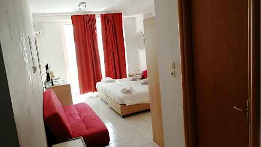 Et hotelværelse med en opredt seng, røde gardiner og en rød sofa. (AI-genereret tekst)