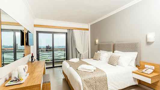 Et hotelværelse med en stor seng, lyse møbler og en balkon med udsigt. (AI-genereret tekst)