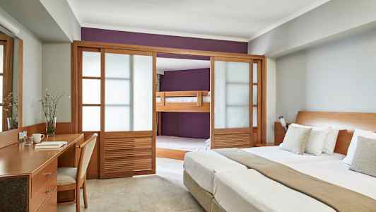 Billede af et hotelværelse med dobbeltseng, skrivebord og en sovealkove med køjeseng bag træskydedøre. (AI-genereret tekst)