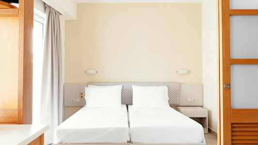 To enkeltsenge med hvidt sengetøj og neutrale møbler. (AI-genereret tekst)