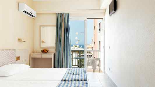 Hotelværelse med to senge, blågule sengetæpper, spejl og en altandør med udsigt. (AI-genereret tekst)