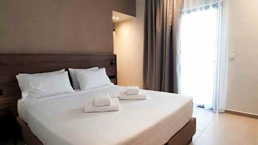 Et hotelværelse med en dobbeltseng og hvide lagner, samt foldede håndklæder placeret på sengen. (AI-genereret tekst)