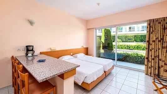 Et hotelværelse med to senge, køkkenbar med siddepladser og stor glasdør mod en have. (AI-genereret tekst)