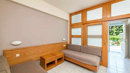 Et værelse med to enkeltsenge og træmøbler, åbner op mod en have. (AI-genereret tekst)