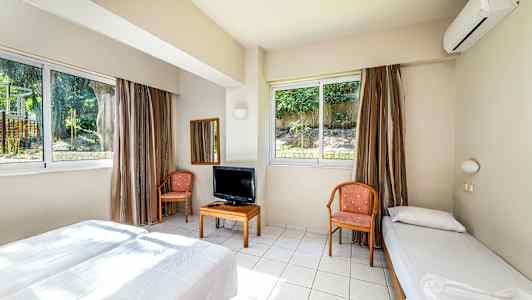 Et hotelværelse med to senge, stole, et bord med fjernsyn og store vinduer. (AI-genereret tekst)