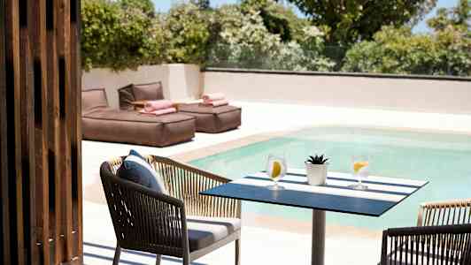 Et bord med to glas vand og en lille plante ved en pool, med liggestole i baggrunden. (AI-genereret tekst)