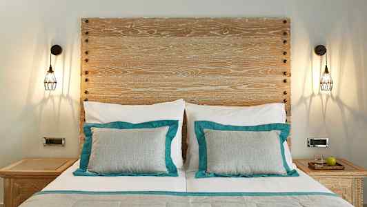 Et værelse med en seng med to puder med turkise detaljer og en træpanel som sengegærde. På hver side af sengen er der natborde med lamper over. (AI-genereret tekst)
