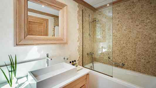 Et badeværelse med en håndvask, et spejl med træramme og et badekar med mosaikvæg og bruser. (AI-genereret tekst)