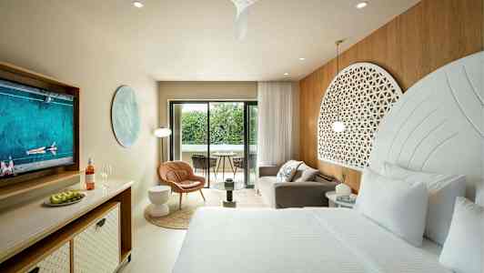 Et elegant hotelværelse med en stor seng, siddeområde og en balkon med udsigt til grønt. (AI-genereret tekst)