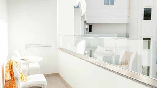 Hvid balkon med glasrækværk, et bord og to stole. (AI-genereret tekst)