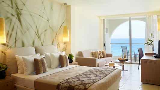 Hotelværelse med havudsigt og moderne indretning, herunder seng, sofa og balkon. (AI-genereret tekst)