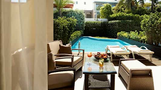 Udsigt over en pool med solsenge og have samt en siddegruppe med bord. (AI-genereret tekst)