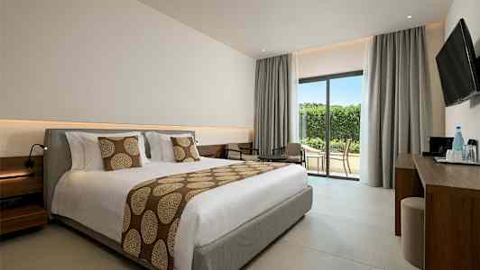 Et hotelværelse med en stor opredt seng, siddegruppe og glasdør mod terrasse. (AI-genereret tekst)