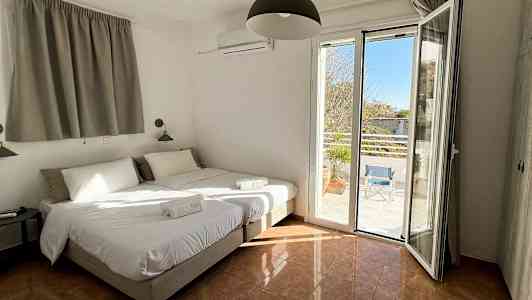 Hotelværelse med to enkeltsenge, åbne vinduer med udsigt til en terrasse. (AI-genereret tekst)