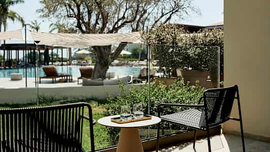 Udsigt til en udendørs pool med stole og planter i forgrunden. (AI-genereret tekst)