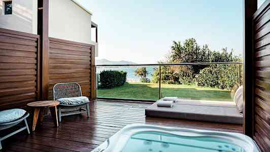 En terrasse med spabad, stole og et bord, udsigt over en grøn græsplæne og havet. (AI-genereret tekst)