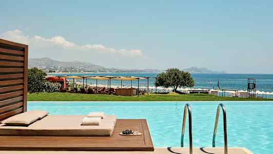 Udsigt fra en pool mod havet, liggestole og parasoller. (AI-genereret tekst)