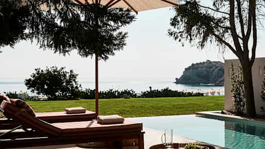 Liggestole ved en pool med udsigt over havet og en klippe. (AI-genereret tekst)