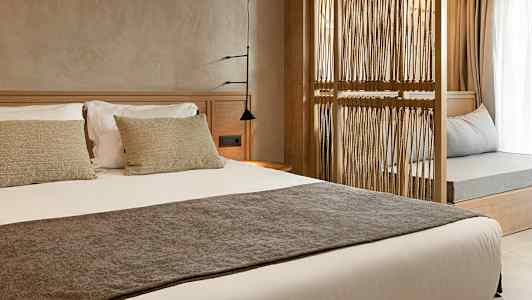 En hotelværelsesinteriør med en redt seng og en dekorativ træramme som adskiller rummet. (AI-genereret tekst)