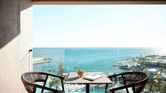 To stole og et bord med en skål og en bog står på en altan med udsigt over havet. (AI-genereret tekst)