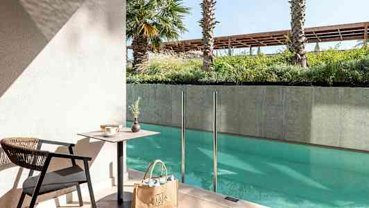 En siddegruppe med bord og stol ved en pool med glasrækværk. (AI-genereret tekst)