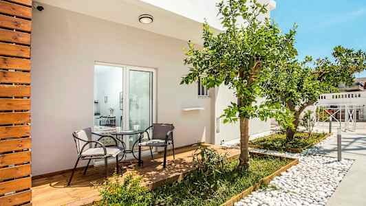 En terrasse med træterrasse og to stole omkring et bord, omgivet af planter og et citrus træ. (AI-genereret tekst)