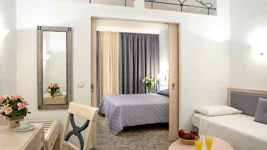 Hotelværelse med to senge, et bord med to glas appelsinjuice og et skrivebord med spejl og blomster. (AI-genereret tekst)