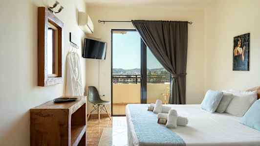Et hotelværelse med en seng, tv, stol og udsigt over en balkon. (AI-genereret tekst)