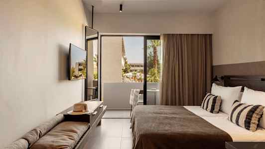 Et hotelværelse med en seng, en bænk med en hat og udsigt til en altan med træer. (AI-genereret tekst)