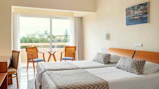 Et hotelværelse med to enkeltsenge, en siddegruppe og udsigt til grønne omgivelser. (AI-genereret tekst)