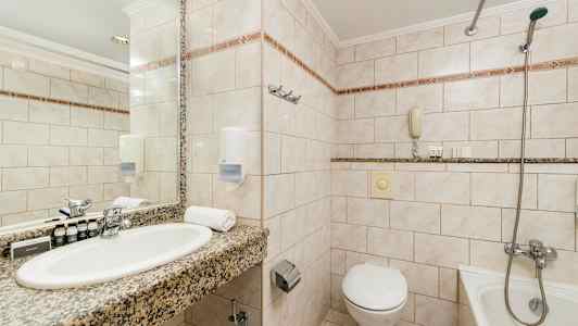 Billede af et badeværelse med håndvask, spejl, toilet og badekar. (AI-genereret tekst)