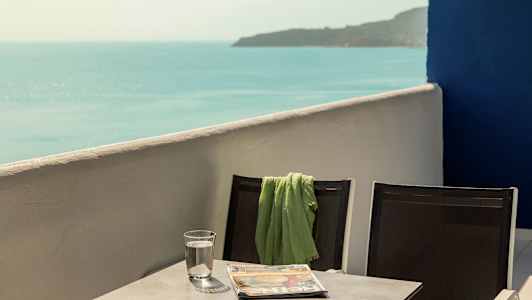 To stole med et grønt tæppe på den ene, stående ved et bord med et glas vand og en avis, med havudsigt. (AI-genereret tekst)